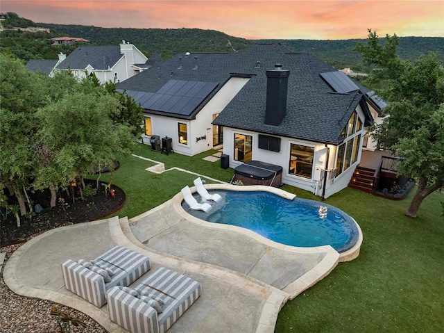 pool at dusk featuring a patio area, a jacuzzi, an outdoor pool, and a yard