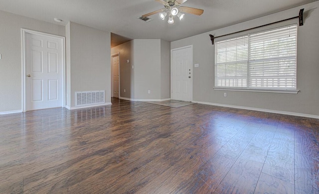 empty room featuring dark wood-type flooring, visible vents, baseboards, and a ceiling fan