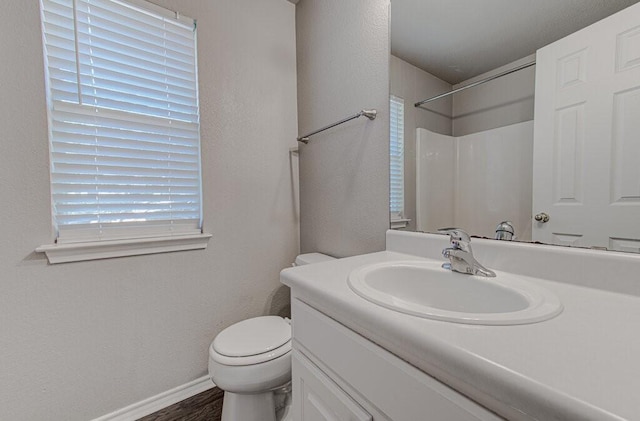 bathroom featuring toilet, wood finished floors, vanity, baseboards, and walk in shower