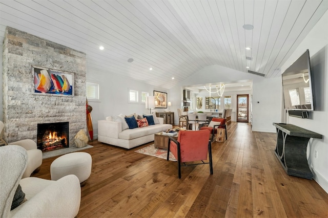 living room with recessed lighting, wood-type flooring, vaulted ceiling, a stone fireplace, and baseboards