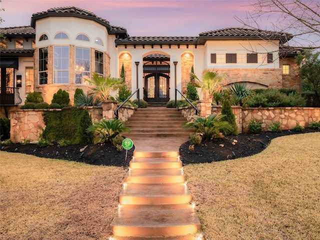 mediterranean / spanish-style house featuring a tiled roof, stucco siding, french doors, and a yard