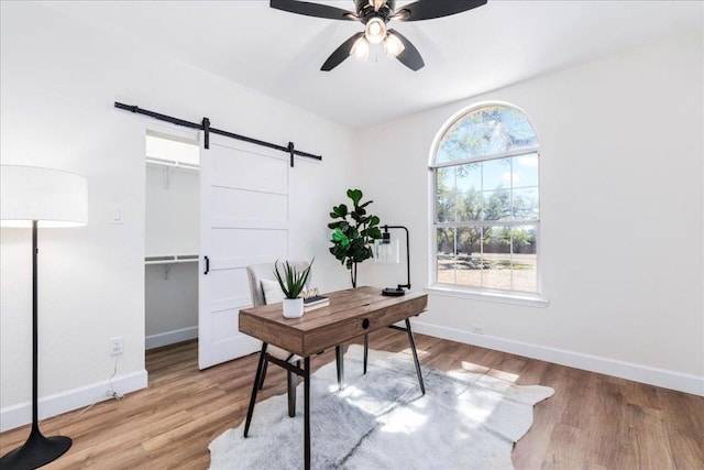 office space featuring a ceiling fan, a barn door, baseboards, and wood finished floors