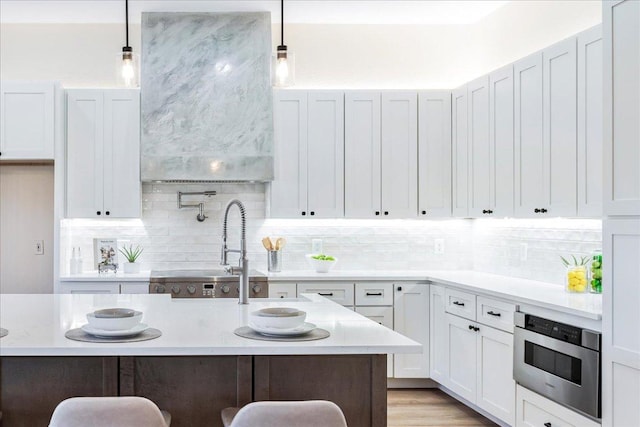 kitchen with tasteful backsplash, white cabinets, a kitchen breakfast bar, decorative light fixtures, and light wood-style floors