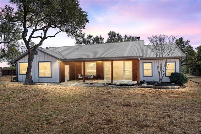 back of house with board and batten siding, metal roof, a lawn, and a patio