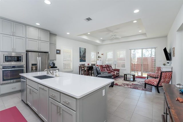 kitchen featuring a sink, a tray ceiling, appliances with stainless steel finishes, and gray cabinets