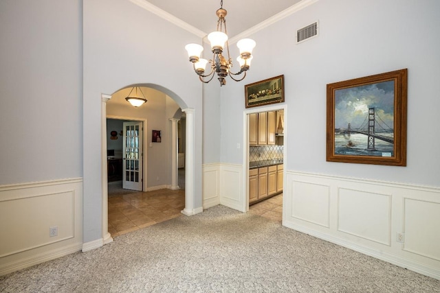 unfurnished dining area featuring arched walkways, a wainscoted wall, visible vents, and light colored carpet