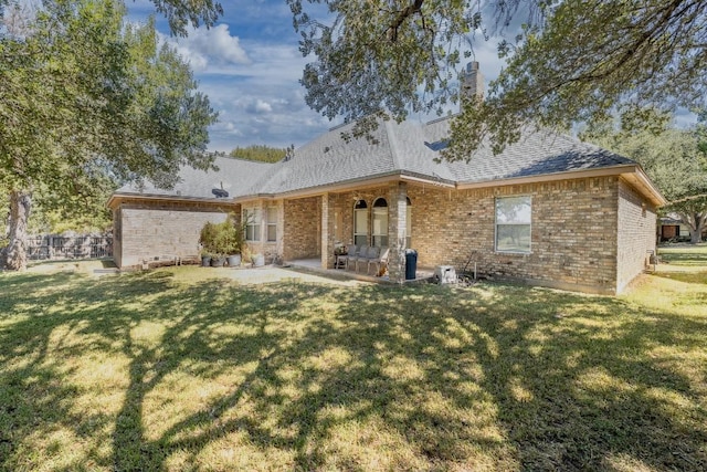 back of property with a shingled roof, a patio area, brick siding, and a lawn