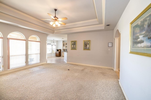 unfurnished living room with a tray ceiling, light colored carpet, crown molding, and arched walkways