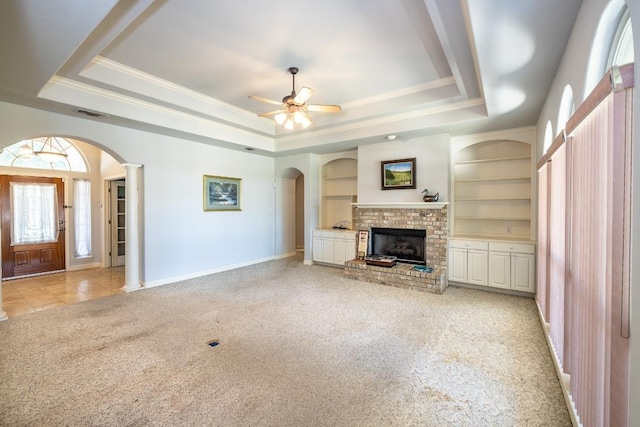 unfurnished living room with arched walkways, a raised ceiling, built in features, and light colored carpet