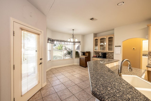 kitchen featuring a chandelier, a sink, visible vents, hanging light fixtures, and glass insert cabinets