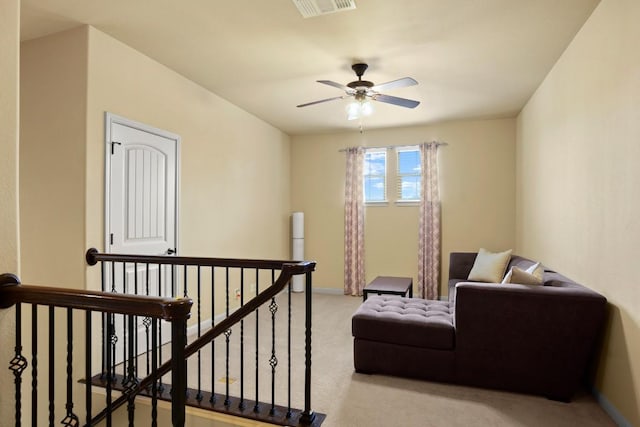 living area with light colored carpet, visible vents, ceiling fan, an upstairs landing, and baseboards