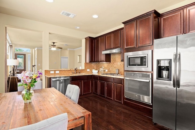 kitchen with under cabinet range hood, stainless steel appliances, wood counters, visible vents, and tasteful backsplash