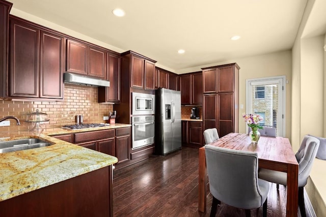 kitchen with under cabinet range hood, dark wood-style flooring, a sink, appliances with stainless steel finishes, and light stone countertops