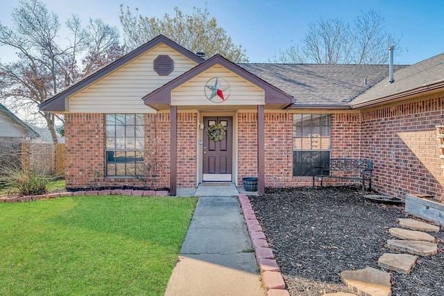 view of front facade with brick siding, a front lawn, a shingled roof, and fence