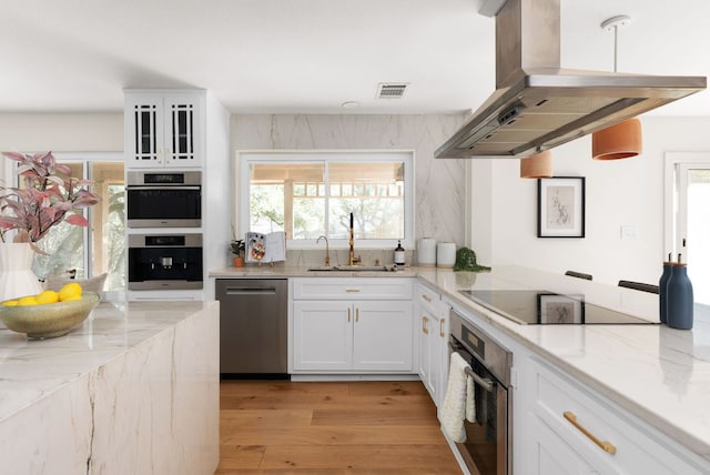 kitchen with stainless steel appliances, white cabinets, a sink, island range hood, and light stone countertops