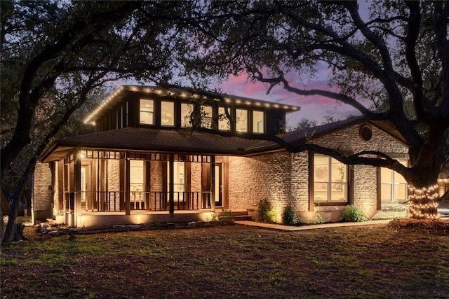 back of property at dusk with stone siding and a porch