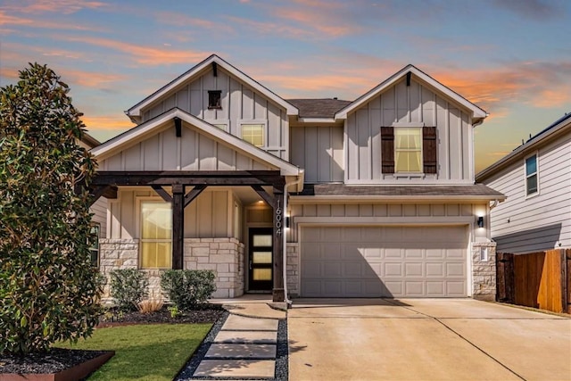 view of front facade featuring a garage, driveway, stone siding, fence, and board and batten siding