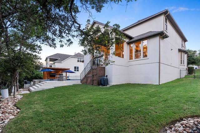 rear view of property with fence, stairway, a lawn, and stucco siding