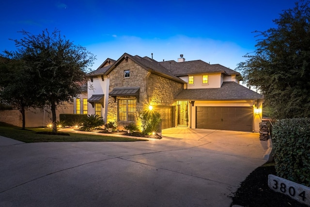 traditional-style house with a garage, driveway, stone siding, a standing seam roof, and stucco siding