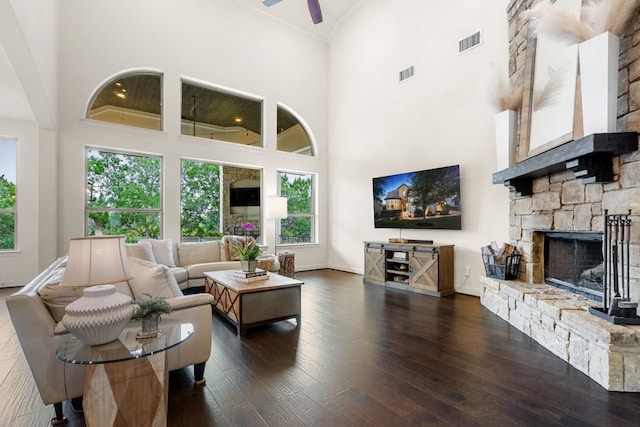 living area featuring dark wood-style floors, visible vents, a stone fireplace, and a towering ceiling