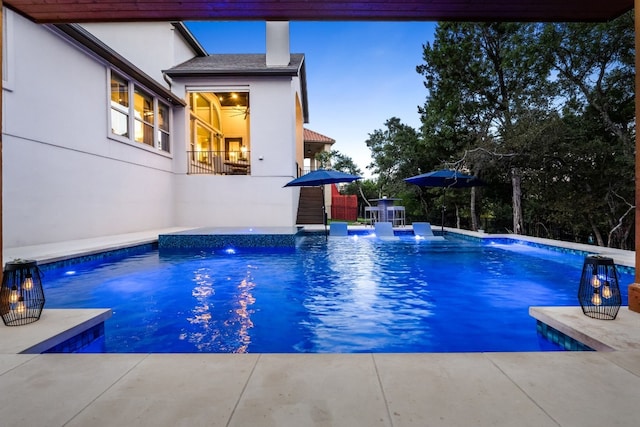 pool at dusk with an outdoor pool and a patio