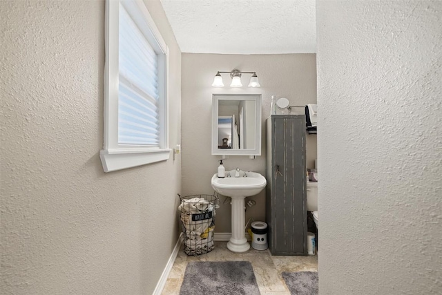 half bathroom featuring a textured ceiling, a textured wall, a sink, and baseboards