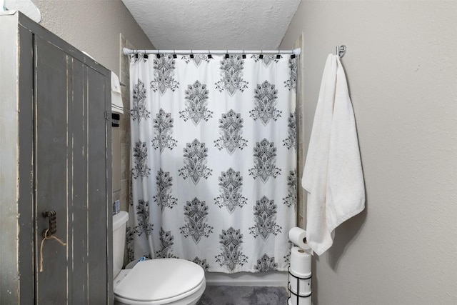 bathroom with a textured ceiling, a textured wall, a shower with shower curtain, and toilet