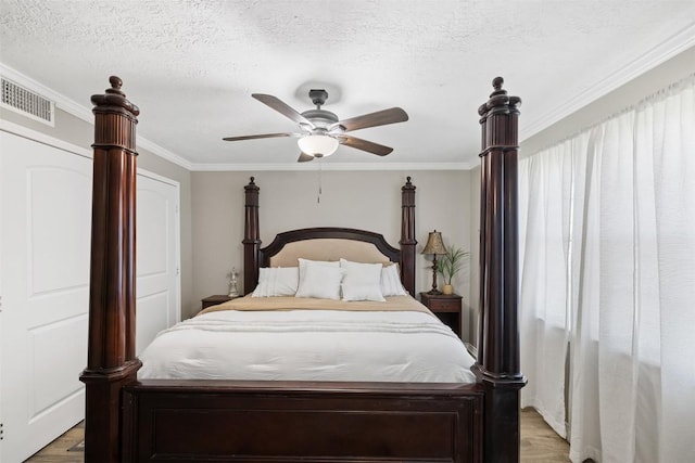 bedroom featuring light wood-style flooring, a textured ceiling, a ceiling fan, and crown molding