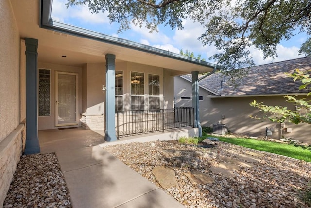 doorway to property with covered porch, roof with shingles, and stucco siding