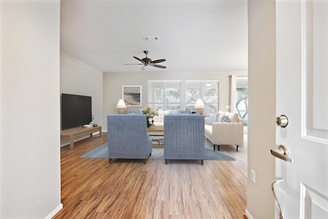 living room featuring a ceiling fan, light wood-type flooring, visible vents, and baseboards