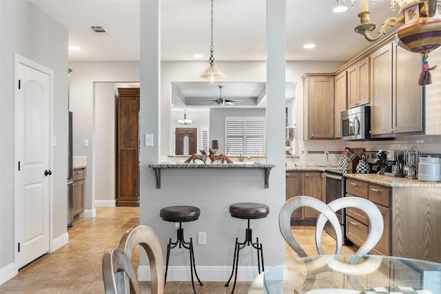 kitchen with light stone counters, a peninsula, visible vents, hanging light fixtures, and appliances with stainless steel finishes