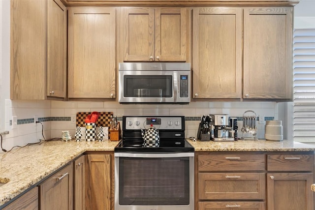 kitchen with appliances with stainless steel finishes, brown cabinetry, light stone counters, and decorative backsplash