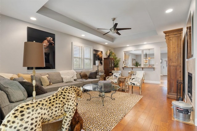 living room with light wood finished floors, recessed lighting, a raised ceiling, a ceiling fan, and baseboards