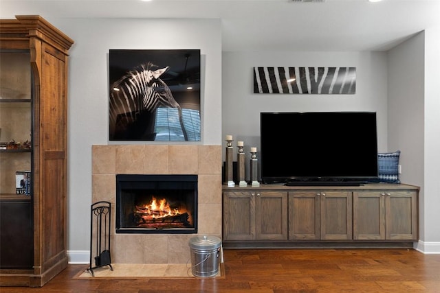 living area with a tiled fireplace, dark wood finished floors, visible vents, and baseboards