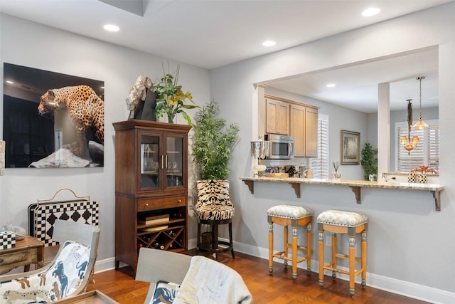 interior space featuring recessed lighting, stainless steel microwave, hanging light fixtures, dark wood-type flooring, and a kitchen bar