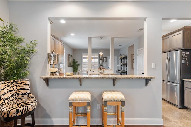 kitchen with a peninsula, light stone countertops, a breakfast bar area, and freestanding refrigerator