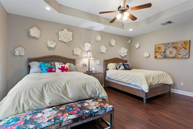 bedroom with baseboards, visible vents, dark wood-type flooring, a tray ceiling, and recessed lighting