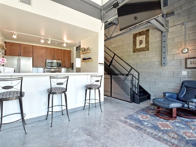 kitchen with brown cabinets, a breakfast bar area, stainless steel appliances, light countertops, and a peninsula