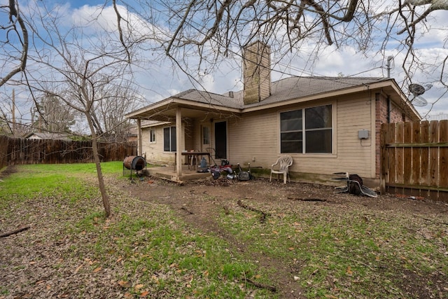 back of house with a fenced backyard, a chimney, heating fuel, a yard, and a patio area