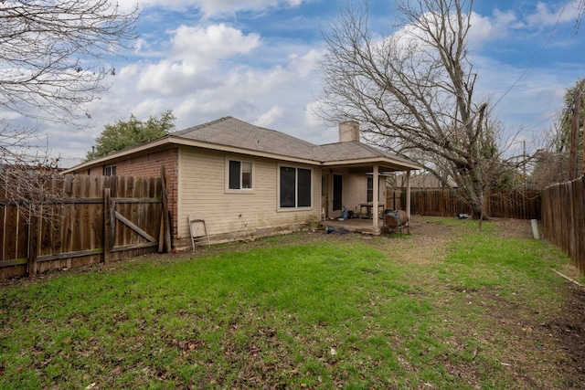 back of property with a fenced backyard, a chimney, a lawn, and a patio