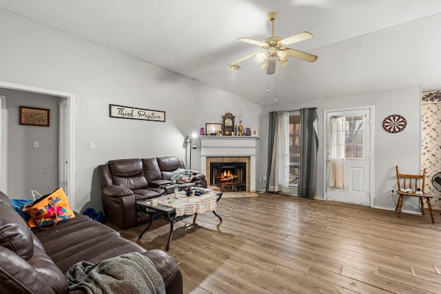 living area with vaulted ceiling, ceiling fan, light wood finished floors, and a tiled fireplace