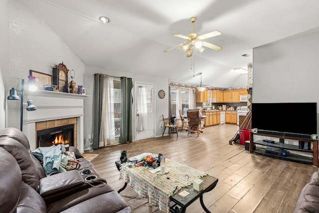 living area featuring a ceiling fan, a tile fireplace, vaulted ceiling, and light wood finished floors