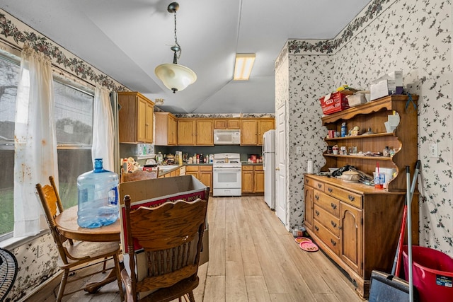 kitchen with decorative light fixtures, light wood-style floors, a sink, white appliances, and wallpapered walls