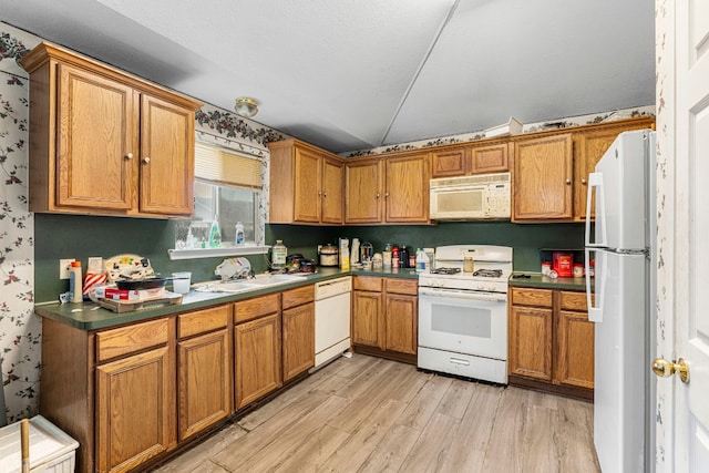 kitchen featuring brown cabinetry, light wood-type flooring, white appliances, and a sink