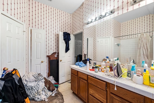 bathroom featuring tiled shower, vanity, and wallpapered walls