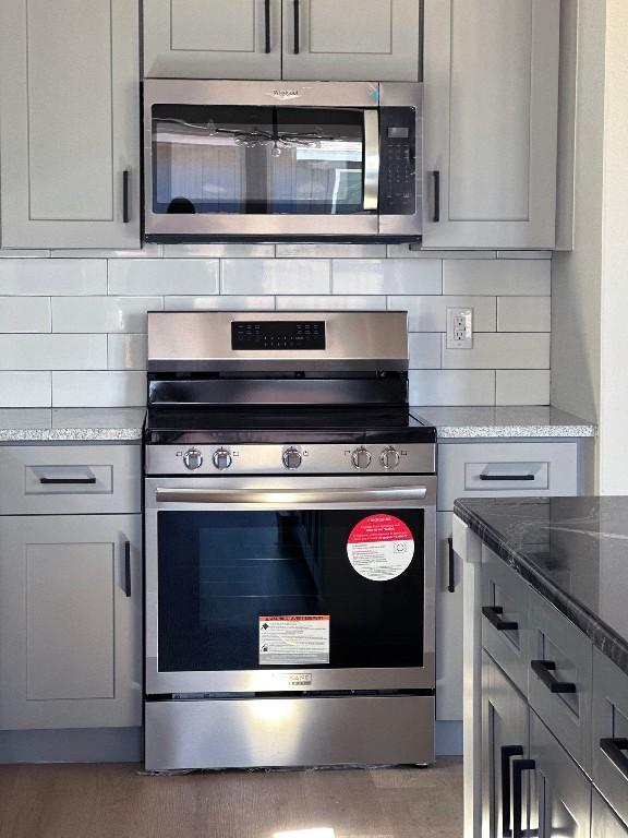 849 Cypress Ln, Cottonwood Shores, TX 78657 - kitchen with stainless steel appliances, gray cabinets, backsplash, and light stone counters