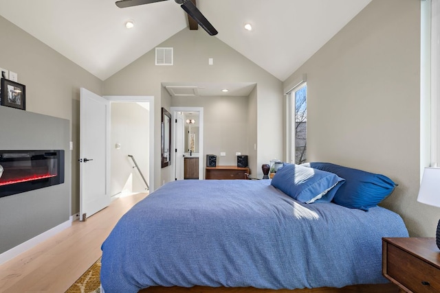 bedroom with light wood finished floors, visible vents, a glass covered fireplace, ceiling fan, and beam ceiling