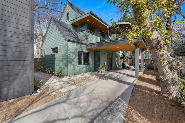 view of front of home with a shingled roof, fence, and a balcony