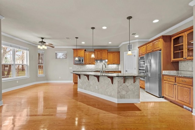 kitchen with brown cabinetry, appliances with stainless steel finishes, a breakfast bar, under cabinet range hood, and a sink