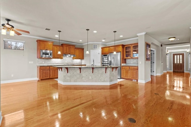 kitchen with a breakfast bar, brown cabinets, visible vents, appliances with stainless steel finishes, and a sink